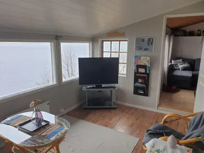 a living room with a flat screen tv and two windows at Idyllic lakeside cabin with private beach and boat in Vassli
