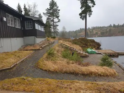 a house sitting next to a body of water at Idyllic lakeside cabin with private beach and boat in Vassli