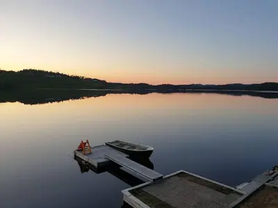 a small boat sitting at a dock on a lake at Idyllic lakeside cabin with private beach and boat in Vassli