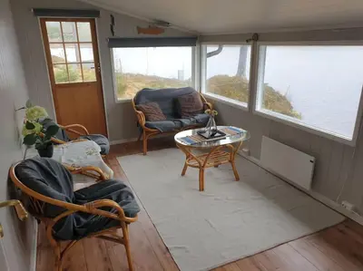 a living room with chairs and a table and windows at Idyllic lakeside cabin with private beach and boat in Vassli