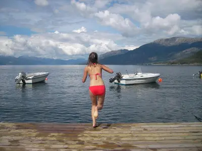 a woman in a bikini walking into the water with boats at Fjordhytte-1 ist eine schöne Hütte bei Ænes am Hardangerfjord mit grandiosem Fjordpanorama, 20 PS Motorboot mietbar in Ænes