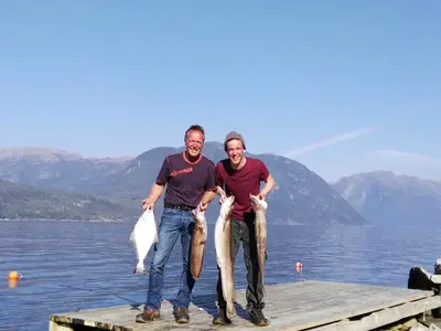 two people standing on a dock with two fish at Fjordhytte-1 ist eine schöne Hütte bei Ænes am Hardangerfjord mit grandiosem Fjordpanorama, 20 PS Motorboot mietbar in Ænes