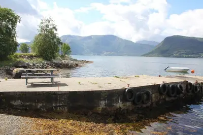a bench on the shore of a lake with a boat at Fjordhytte-39 am Hardangerfjord, Motorboot mietbar in Rosendal