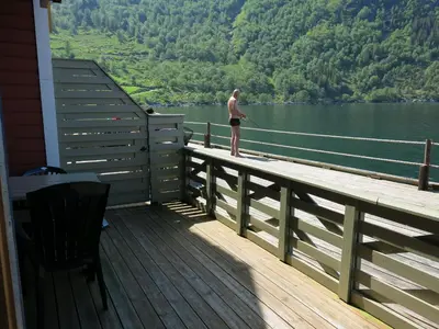 a man is standing on a dock fishing on a lake at Fjordhytte-16 direkt am Sognefjord in Bjordal, mit mietbaren 9,9 PS bis 60 PS Motorbooten in Bjordal