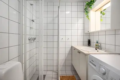 a white tiled bathroom with a shower and a sink at Studio in the city centre in Trondheim