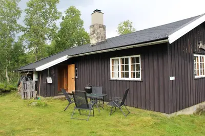 a black house with chairs and a table in front of it at Jonstølen by Norgesbooking - cabin at 1020 masl in Trondsgard
