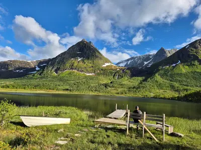 a man sitting on a dock next to a boat on a lake at Hytta på Kvia, Rognestøyldalen - Sæbø in Sæbø