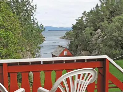 a red bench on a balcony with a red house on the water at Holiday Home Laksevågen by Interhome in Bruntveit