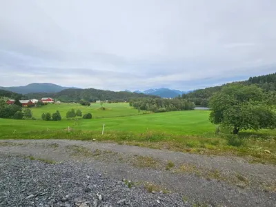 a gravel road with a green field and mountains in the background at Gårdsidyll i flotte omgivelser in Ålesund