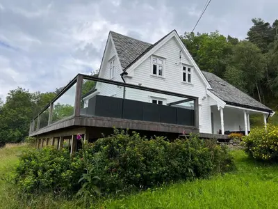a white house with glass windows on the front of it at Fjord house with a private bay, boats and sauna! in Etnesjøen