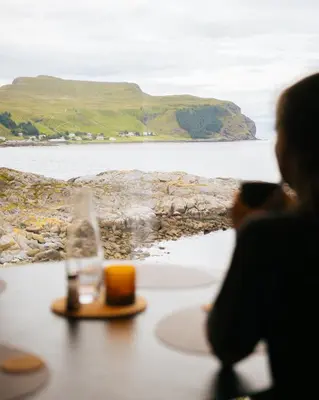 a woman sitting at a table looking out at the ocean at Runde Panorama - Highlight View in Runde