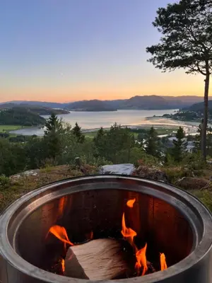a fire pit on a hill with a view of a lake at Speilsuite med egen badstue og panorama in Steinkjer