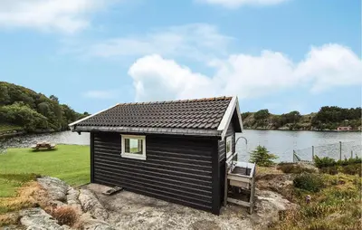a small black house with a bench next to a river at Amazing Home In Haugesund in Haugesund