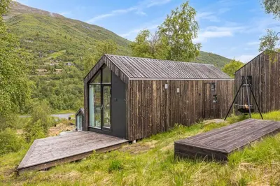a wooden house in a field with mountains in the background at Tiny Mountain Cabin II in Stranda