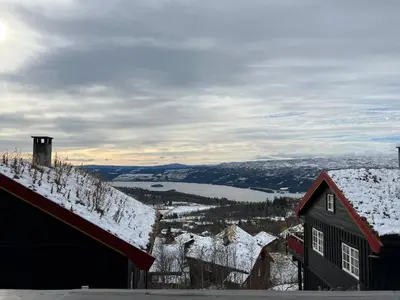 a snow covered mountain with a house and a lake at Cozy apt with a view in Beitostøl