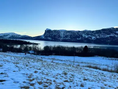 a snowy field with a lake and mountains in the background at Øen Hytter - Hytte 2 in Sørbø