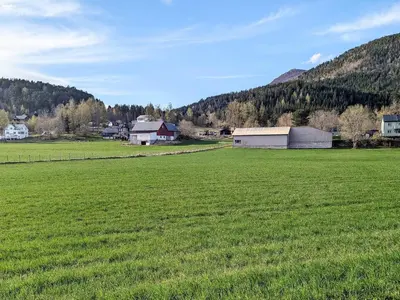 a large field of green grass with houses and a barn at 8 person holiday home in isfjorden-By Traum in Torvik