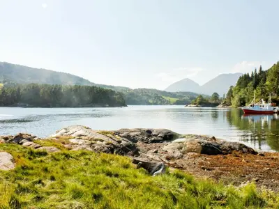 a boat on a river with mountains in the background at 5 person holiday home in VÅGLAND in Bårdset