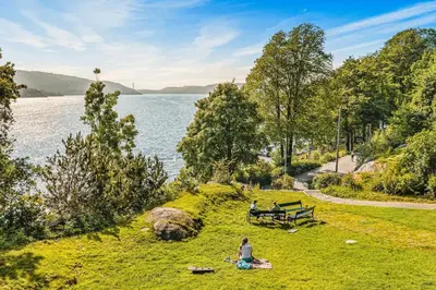 two people sitting in the grass near a lake at 500 m til Bryggen I Skjermet Uteplass! in Bergen