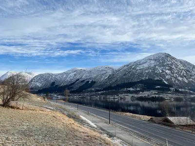a road with snow covered mountains and a body of water at Husslåttene apartments with terrace in Skei