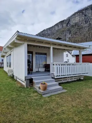 a small white house with a porch and a mountain at Feriehus ved fjorden i Solvorn in Luster