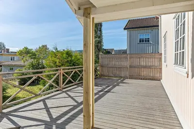 a deck with a wooden railing and a blue house at Sentral leilighet i klassisk hus! in Lillehammer