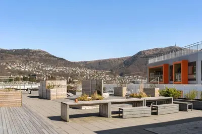 a patio with benches and a building with mountains in the background at Modern Apartment with Rooftop Terrace and Stunning Views in Bergen