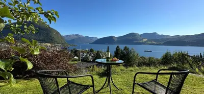 a table and two chairs in the grass near a lake at Cozy Cabin in Volda