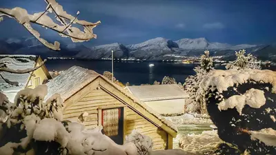 a house covered in snow with a lake and mountains at Cozy Cabin in Volda