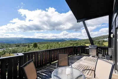 a deck with a glass table and chairs on a balcony at Stølstunets toppetasje in Beitostøl