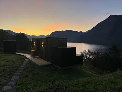 a cabin with a view of a lake at sunset at Glimre Romsdal - Eksklusivt speilhus ved Åndalsnes in Isfjorden