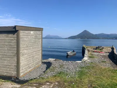 a small building on the shore of a body of water at Villa med sauna ute, egen båt, naust og kai in Breidvik