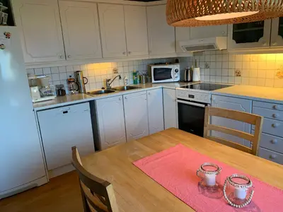 a kitchen with a wooden table and a kitchen with white cabinets at Villa med sauna ute, egen båt, naust og kai in Breidvik
