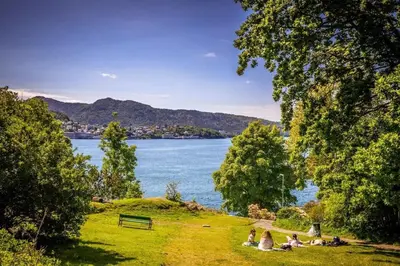 a group of people sitting on the grass near a lake at Dinbnb Appartments l Traditional bergenshouse I Charming I Familiy in Bergen