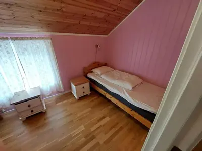 a bedroom with a bed with pink walls and wooden floors at Jovollstua i Eresfjord med båt til leie in Øverås