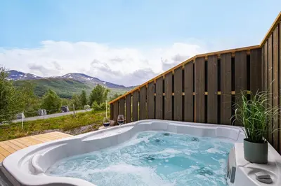 a hot tub on a deck with mountains in the background at Moderne hytte på Fjellsætra med Jacuzzi in Sykkylven