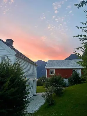 a house and a barn with a sunset in the background at Nyrestaurert hus fra 1700-tallet in Bjørgo