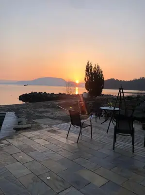 a sunset over the water with chairs and a table at Moderne Rorbu helt i sjøkanten in Hauge