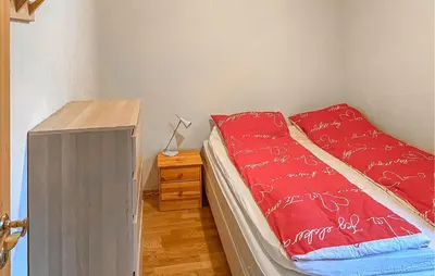 a bedroom with a bed with red sheets and a wooden cabinet at 4 Bedroom Awesome Home In Luster in Luster