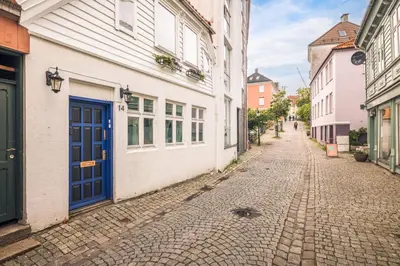 an empty street with white buildings and a blue door at Bergen City Center Bryggen in Bergen