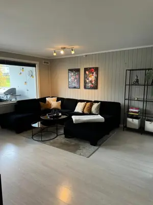 a living room with a black couch and a table at Leilighet nært Granåsen skisenter in Trondheim
