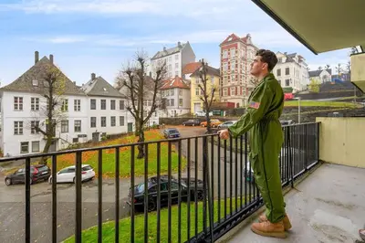 a man standing on a balcony looking out at a city at Dinbnb Apartments l Free Parking l 5 Min From Torget l Nearby Coast I Newly Furnished in Bergen