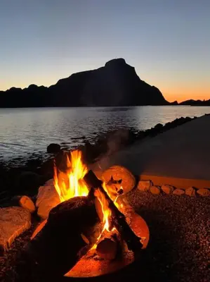 a campfire on the beach with a mountain in the background at Exclusive fjord getaway with sauna in Leirgulen