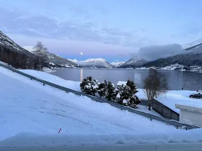 a snow covered field with trees and a body of water at Idyllisk hus i Vassenden sentrum in Vassenden