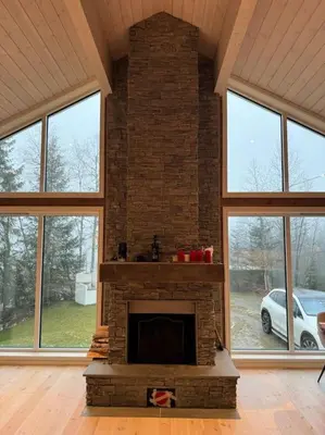 a living room with a brick fireplace with windows at Skogshytte på Skreia in Brattlia