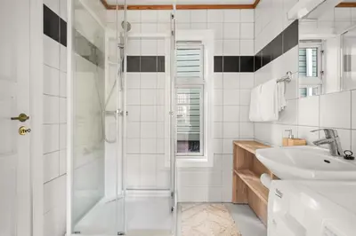 a white bathroom with a shower and a sink at Bryggen Historical Townhouse I Rooftop Views! in Bergen
