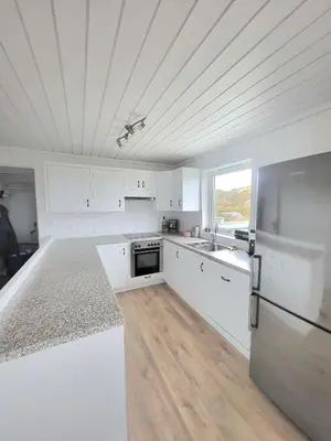 a white kitchen with white cabinets and a refrigerator at Stor hytte med fantastisk utsikt in Vikso