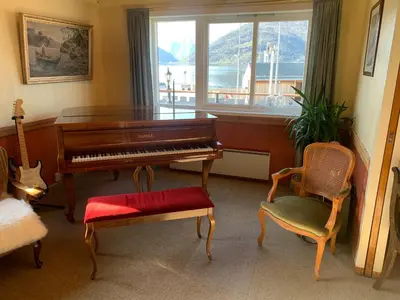 a living room with a piano and a chair and a window at Sognefjord Gjesteheim in Vangsnes