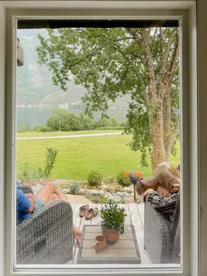 a window with two people sitting on chairs on a patio at Cozy Modern Cabin In West Norway With View in Davik