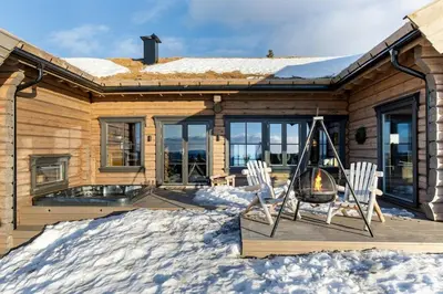 a house with two chairs and a fireplace in the snow at Modern And Spacious Cabin At Mosetertoppen in Øyer